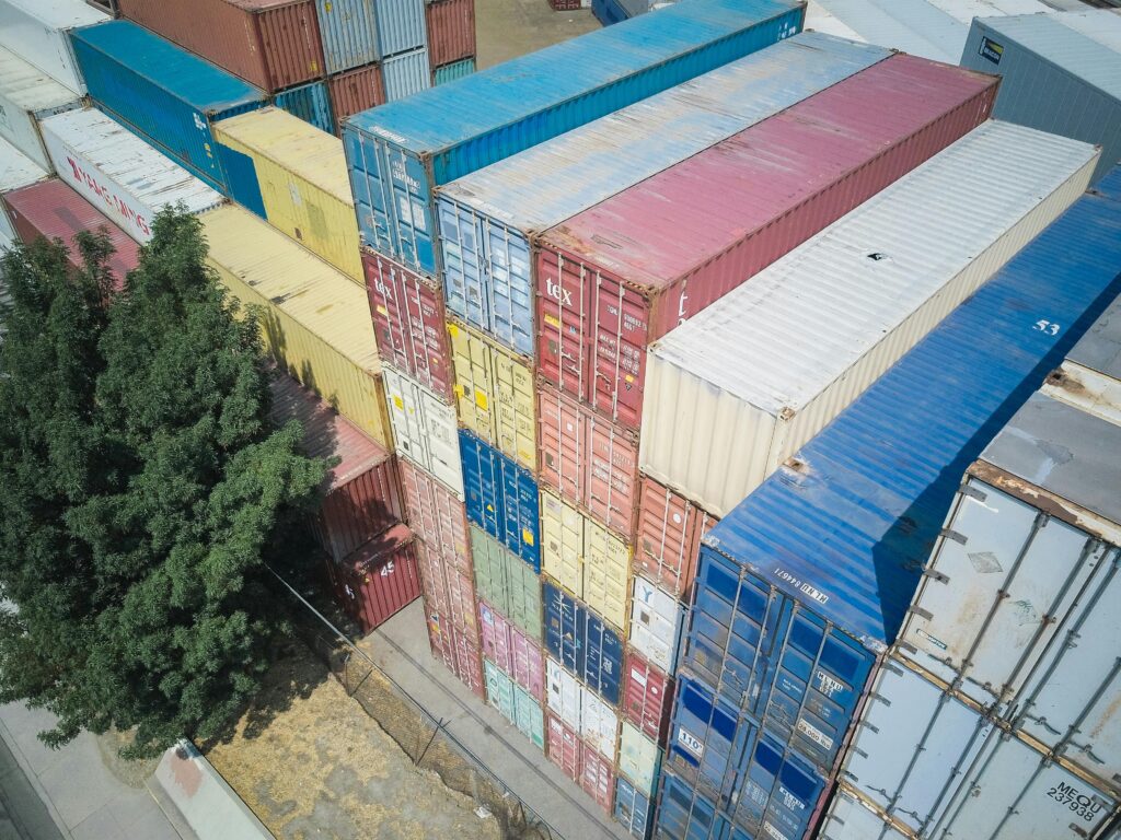 An aerial shot of multi-colored stacked shipping containers near a tree.